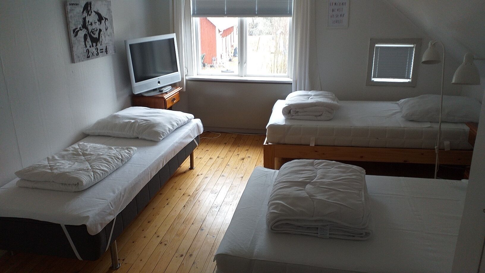 A room with two single beds, a TV on a wooden table, and a window with blinds.