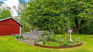 Una baracca rossa, aiuole rialzate in legno e un giardino circolare con un segnale.