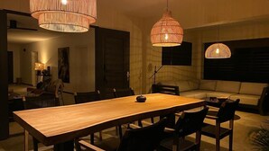 A dining area with a wooden table and chairs, two hanging wicker chandeliers, and a sofa in the background. - Belnem Garden Residence (Kralendijk)