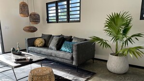 A modern living room with a grey sofa, a large potted plant, and hanging woven light fixtures. - Belnem Garden Residence (Kralendijk)
