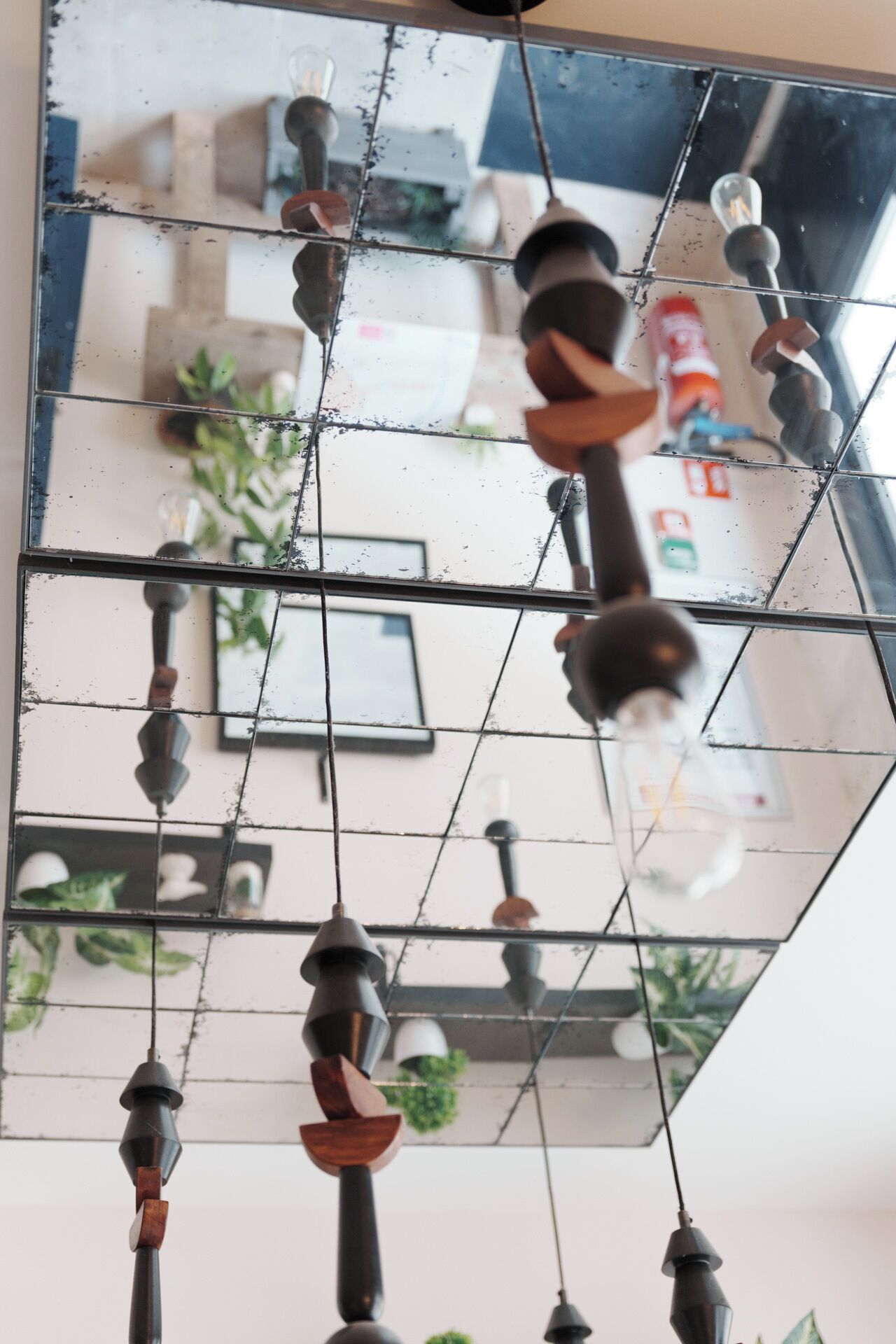 Una habitación con un espejo grande que refleja una zona de cocina, un lámpara colgante y una planta.