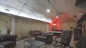Un amplio salón con sofás de cuero, una mesa de centro y un sillón mecedora. Un letrero de neón dice 'Home of Underground'.