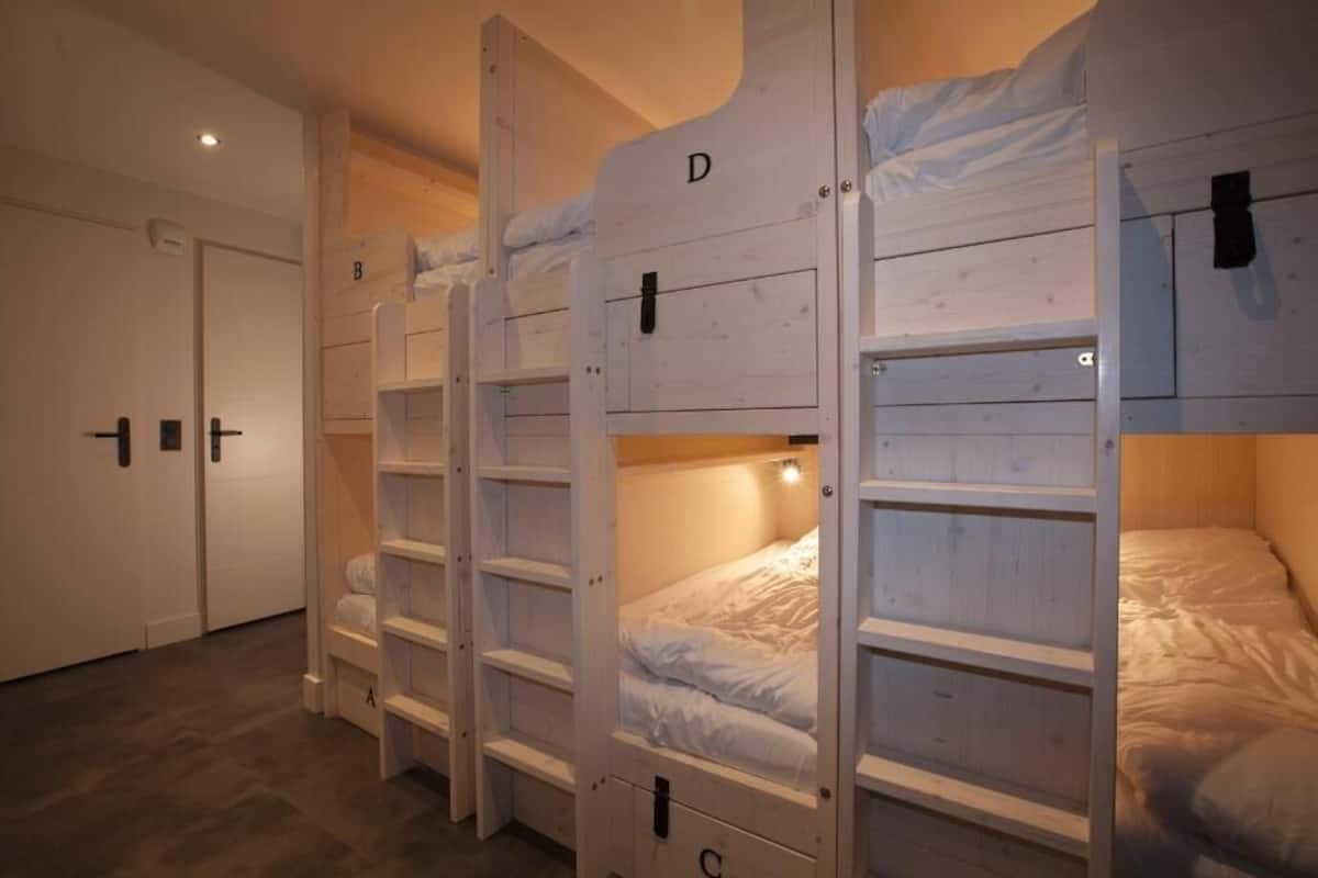 A row of bunk beds labeled A, B, C, and D in a room with white walls and a wooden floor.