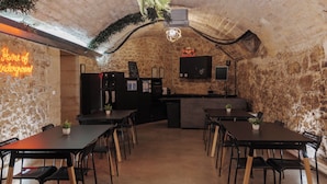 Un restaurante con paredes de piedra, un letrero de neón, una zona de bar y varias mesas y sillas.