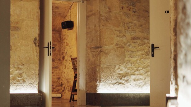 Un pasillo con paredes de piedra y vigas de madera, que conduce a dos puertas con la etiqueta 'CH'.