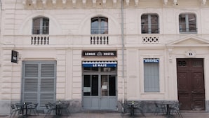 Un edificio con un letrero que dice 'LE MAJE HOSTEL' y 'LE MAJE' restaurante. Hay mesas y sillas al aire libre al frente.