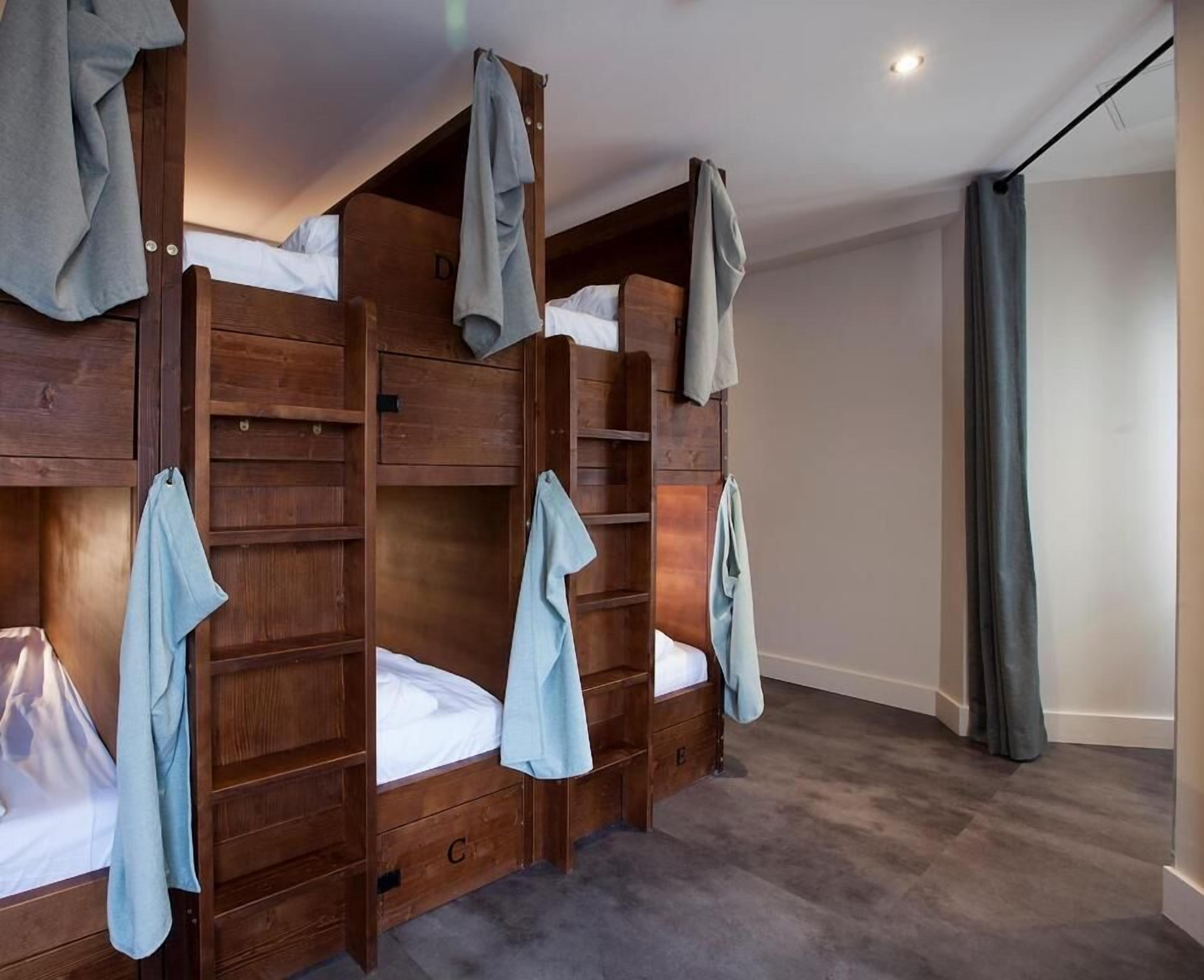 A room with bunk beds, wooden headboards, and a grey curtain.
