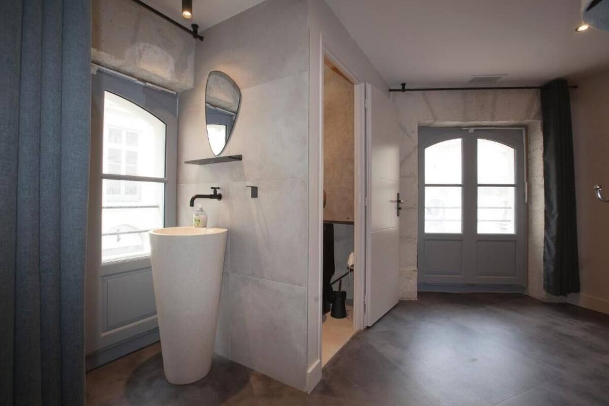 A modern bathroom with a large white sink, a mirror, and a door leading to another room.