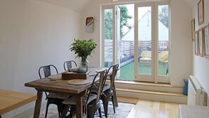 A dining area with a wooden table, chairs, a vase with a plant, and a view of a backyard through glass doors. - Beaufort House, Lymington Town Centre (Lymington)