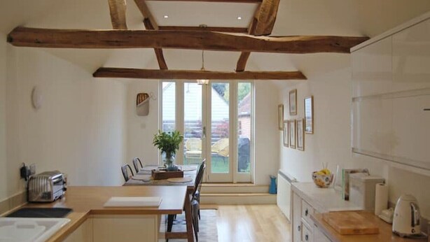 A modern kitchen with wooden beams, a dining area with a table and chairs, and a view through large windows. - Beaufort House, Lymington Town Centre (Lymington)