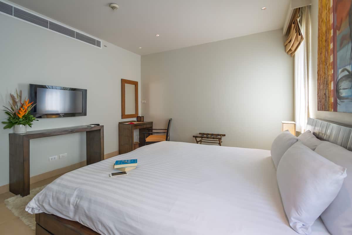 A hotel room with a large bed, a desk with a chair, a TV mounted on the wall, and a window with curtains.