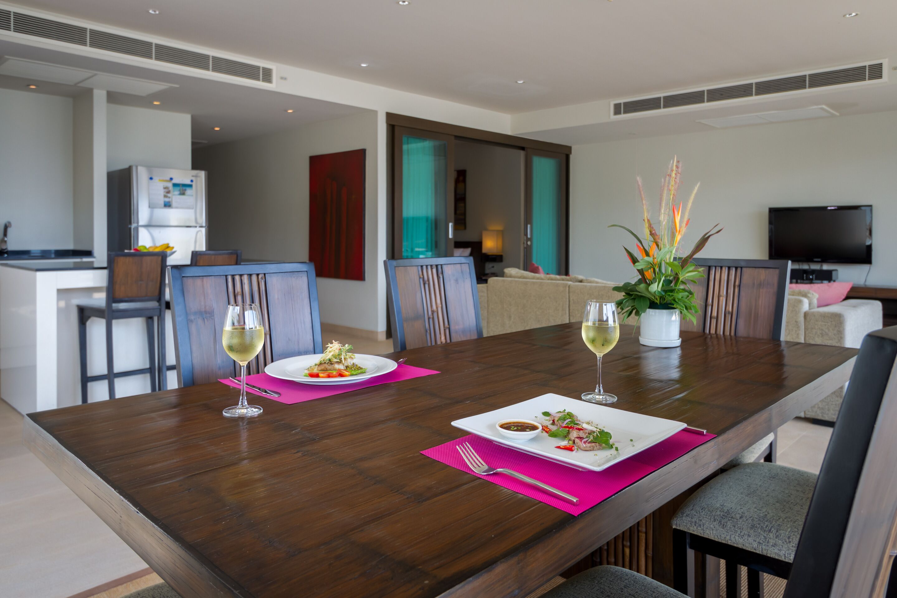 A modern dining area with a wooden table, two plates of food, and wine glasses.