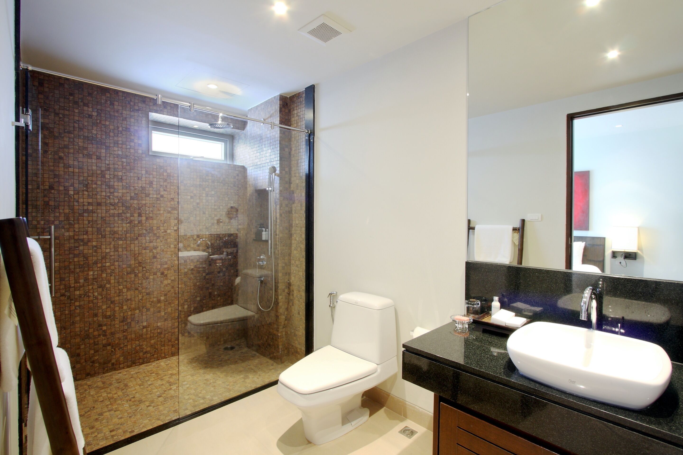 A modern bathroom with a glass-enclosed shower, a white toilet, and a large mirror above a black countertop sink.