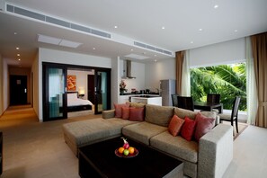 A modern hotel room with a living area, kitchenette, and a large window with a view of greenery.