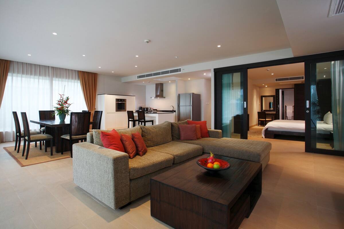 A modern hotel room with a sofa, dining table, and a kitchen area.