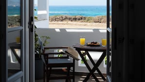 An open door leading to a balcony with a table and chairs, overlooking a beach and ocean. - Sea Lilies Suites (Naxos)