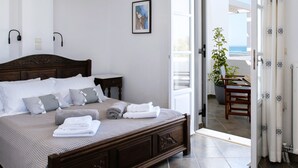 A neatly made bed with white and gray linens, a wooden headboard, and a modern pendant light. - Sea Lilies Suites (Naxos)