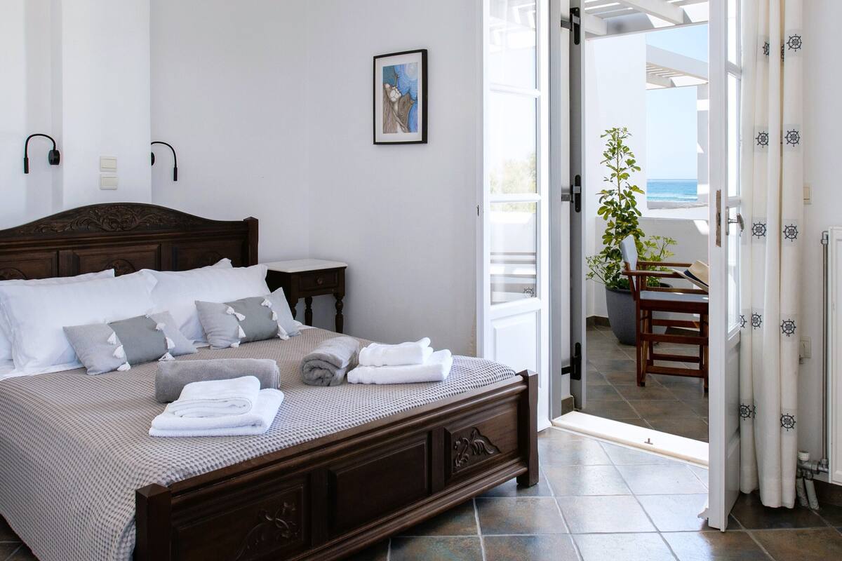 A neatly made bed with white and gray linens, a wooden headboard, and a modern pendant light.