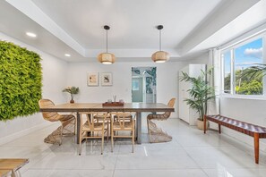 A modern kitchen with a central island, wicker chairs, pendant lights, and a green wall.