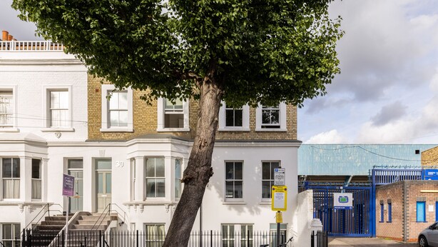 A multi-story building with a white facade, a tree in front, and a bicycle parked on the sidewalk. - Luxurious Villa in Shepherd's Bush (London)