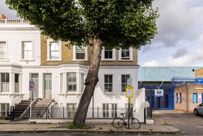 A multi-story building with a white facade, a tree in front, and a bicycle parked on the sidewalk.