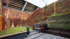 A patio area with a wooden deck, outdoor seating, and a brick wall covered in ivy. - Luxurious Villa in Shepherd's Bush (London)