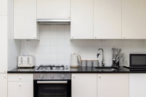 Ett modernt kök med vita skåp, en gasspis, en brödrost, en vattenkokare och en mikrovågsugn.