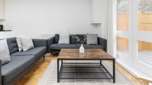 A modern living room with a grey sofa set, a wooden coffee table, and a white vase with branches. - Luxurious Villa in Shepherd's Bush (London)