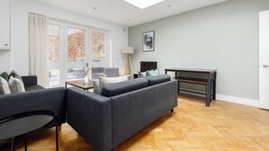 A modern living room with a grey sofa, a small table, and a lamp. - Luxurious Villa in Shepherd's Bush (London)