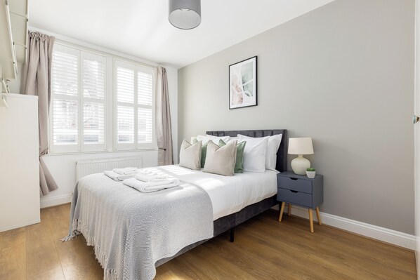 A bedroom with a bed, bedside table, lamp, and a framed picture on the wall.