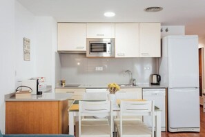 A compact kitchen with white cabinets, a microwave, a sink, and a refrigerator. There is a small dining area with a table and chairs.