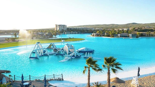 A resort with a large swimming pool, palm trees, and a beach area.