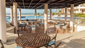 An outdoor pool area with lounge chairs and tables, a covered patio, and a view of the ocean.