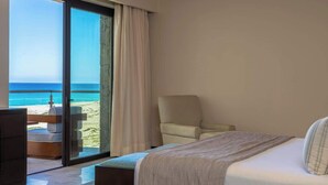 A hotel room with a bed, a chair, a desk, and a view of the beach and ocean through a large sliding glass door.