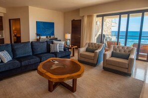 Un salon comprenant un canapé, des fauteuils, une table basse, un tableau et une vue sur l’océan.
