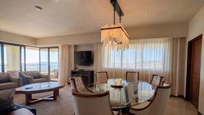 Una sala de estar moderna con una mesa de comedor de vidrio, asientos cómodos, un televisor grande y vistas al exterior.