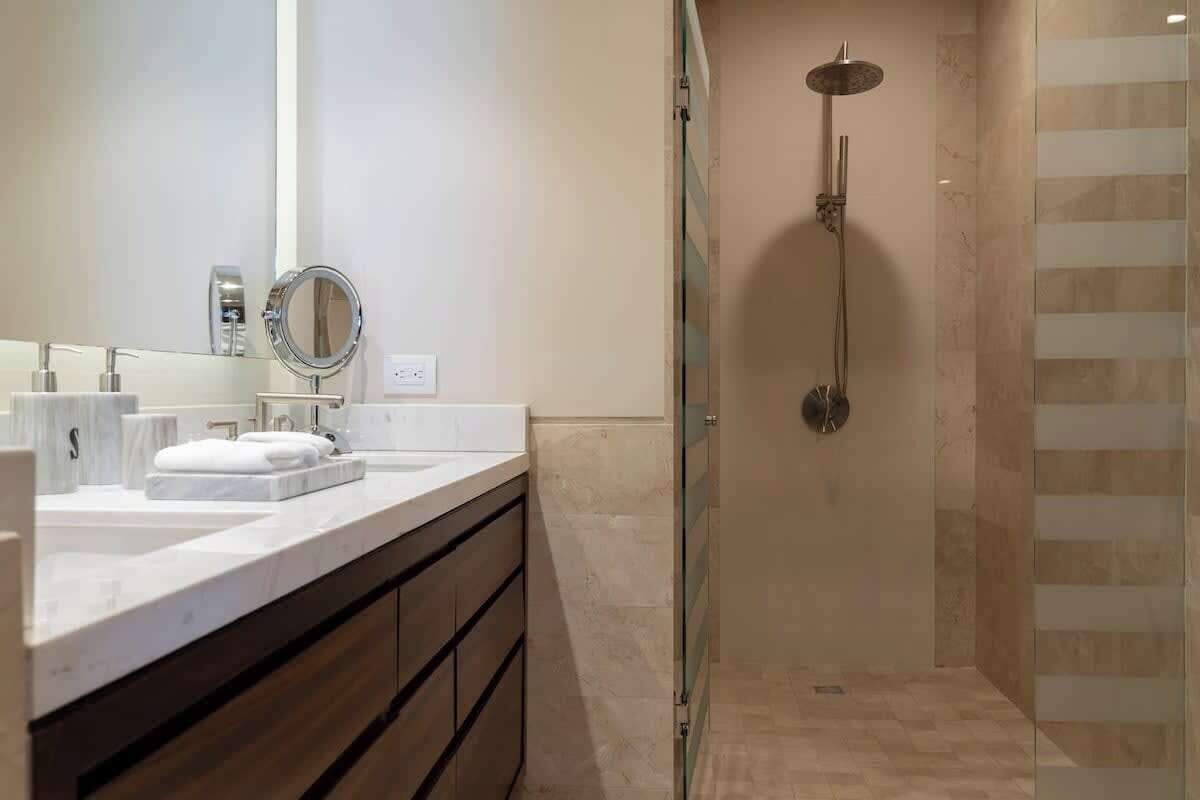 Un baño moderno con cabina de ducha de vidrio, tocador con espejo y suelo de mármol.