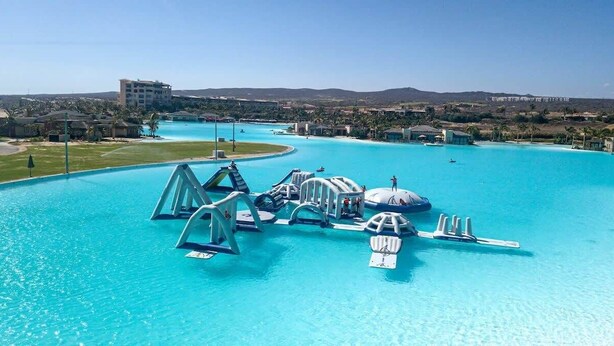 Una gran piscina al aire libre con toboganes y fuentes, rodeada de edificios y un cielo despejado.