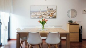 A dining area with a wooden table, two chairs, a vase of flowers, and a painting of a cityscape on the wall. - 2 bedroom apartment RM7 (Girona)