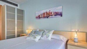 A hotel room with a bed, a nightstand with a lamp, a wall-mounted painting, and a wardrobe. - 2 bedroom apartment RM7 (Girona)