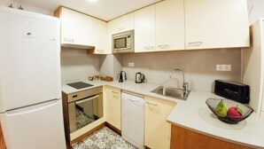 A compact kitchen with white cabinets, a microwave, a sink, a dishwasher, and a small countertop with a fruit bowl. - 2 bedroom apartment RM7 (Girona)