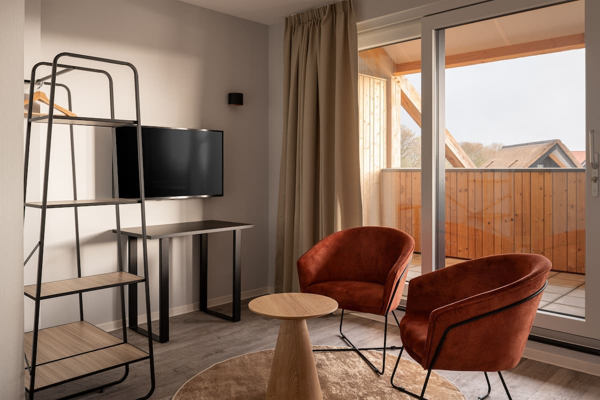 Una sala de estar moderna con televisor, un mueble bajo para la televisión de madera, dos sillones rojos, una mesa de centro redonda y un ventanal corredero que da a un balcón.