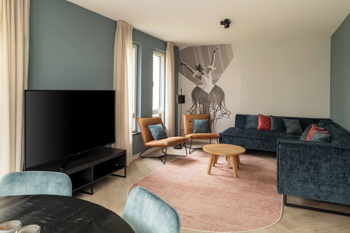 Una sala de estar moderna con un televisor de pantalla plana, dos sillones, un sofá y una mesita de centro.