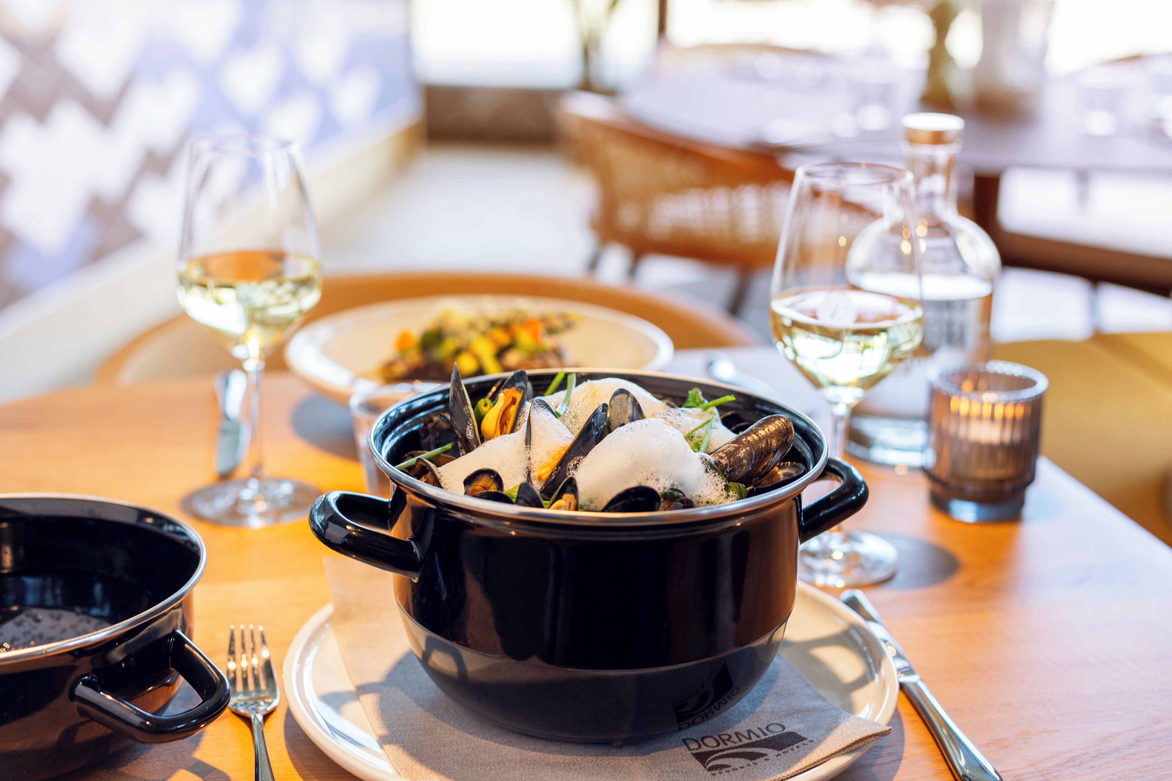A dining table with a black pot of seafood, a plate of food, a wine glass, and a candle.