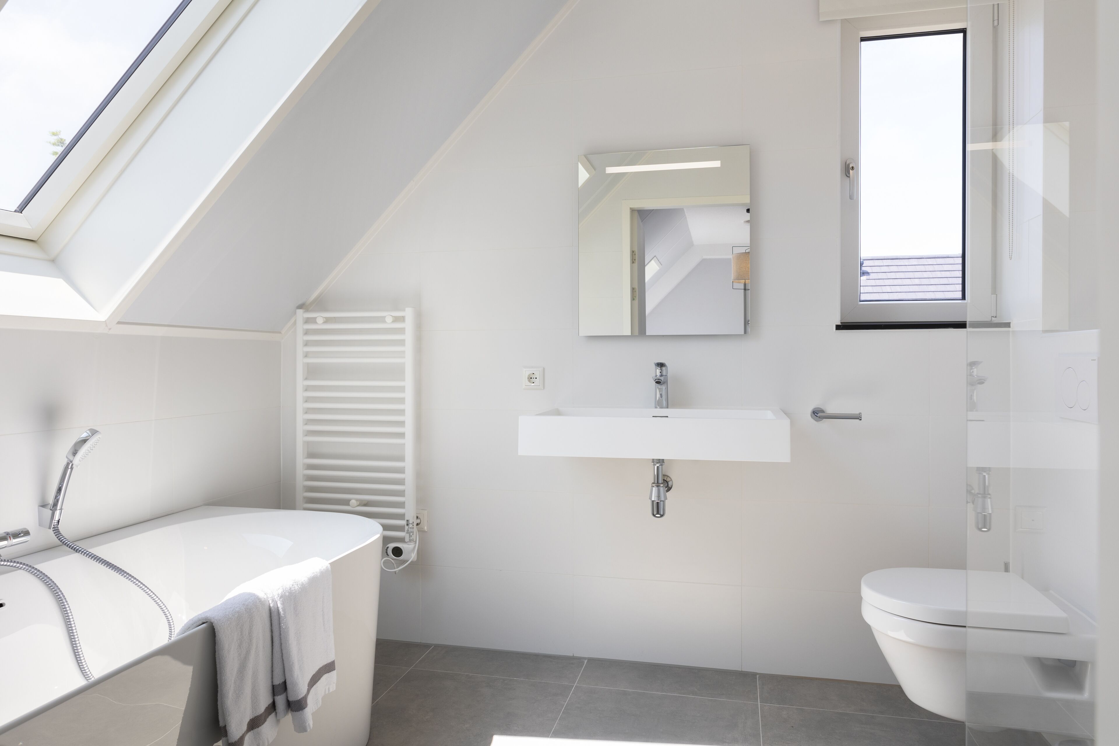 Une salle de bain moderne dotée d’un puits de lumière, d’une baignoire sur pieds, d’un lavabo mural et de toilettes.