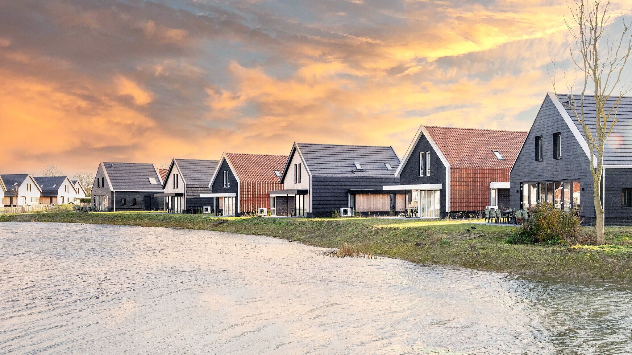 Una hilera de casas modernas con techos inclinados, un área verde al frente y un cielo nublado.