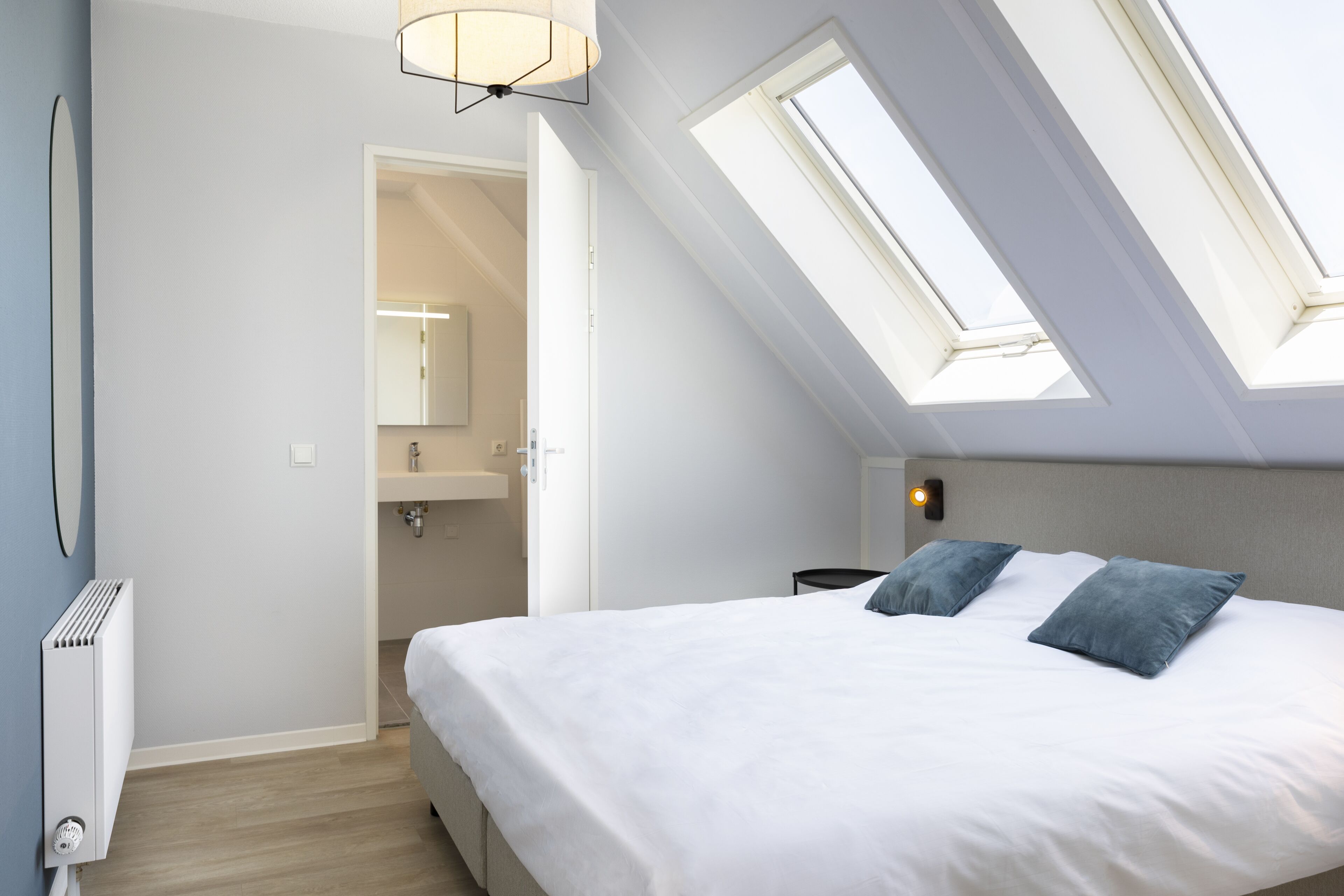 A bedroom with a skylight, a bed with white bedding, a bedside table, and a nightstand.