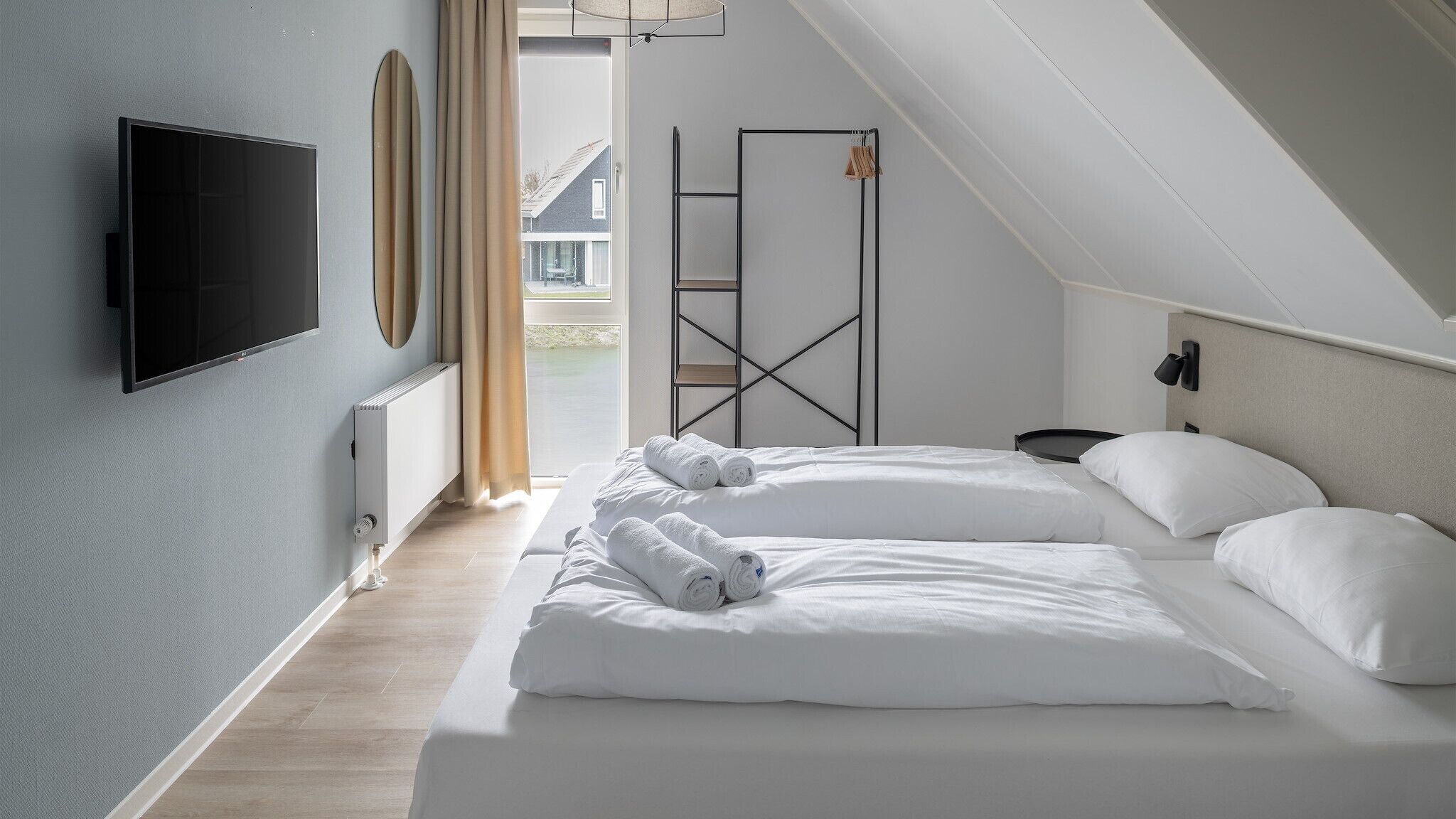 Ein modernes Hotelzimmer mit einem großen Bett, einem an der Wand befestigten Fernseher und Blick ins Freie.