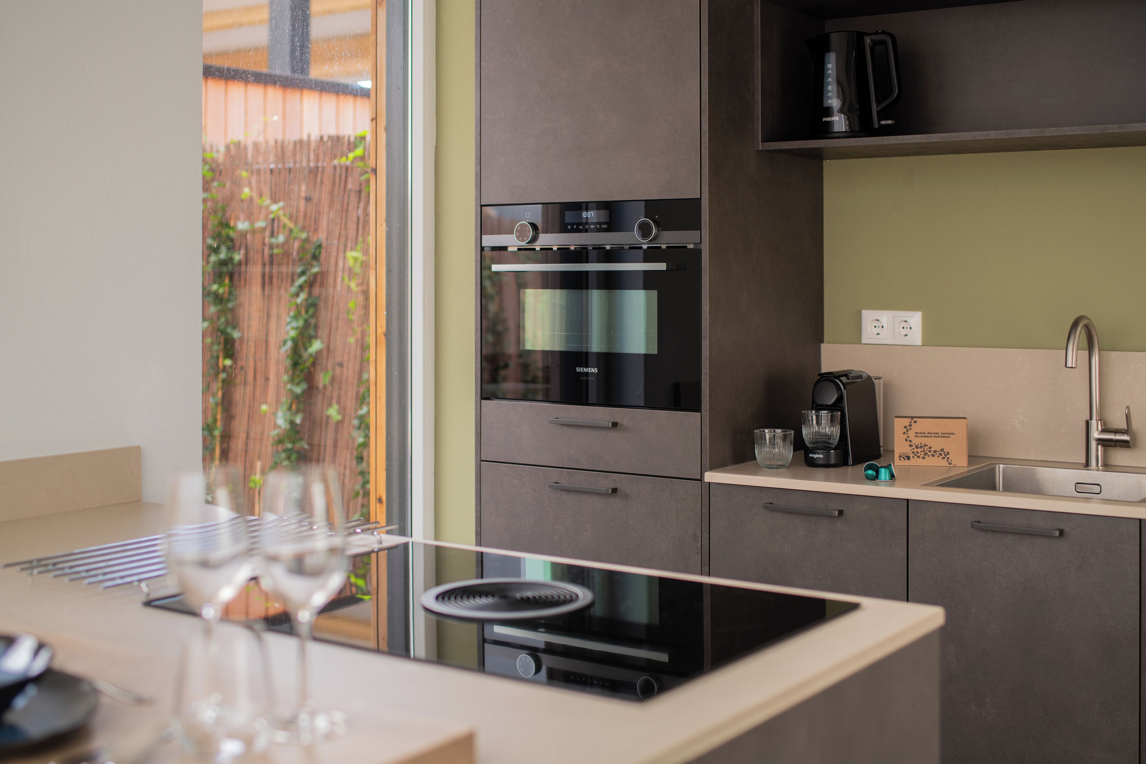 A modern kitchen with built-in appliances, a sink, and a window overlooking a garden.