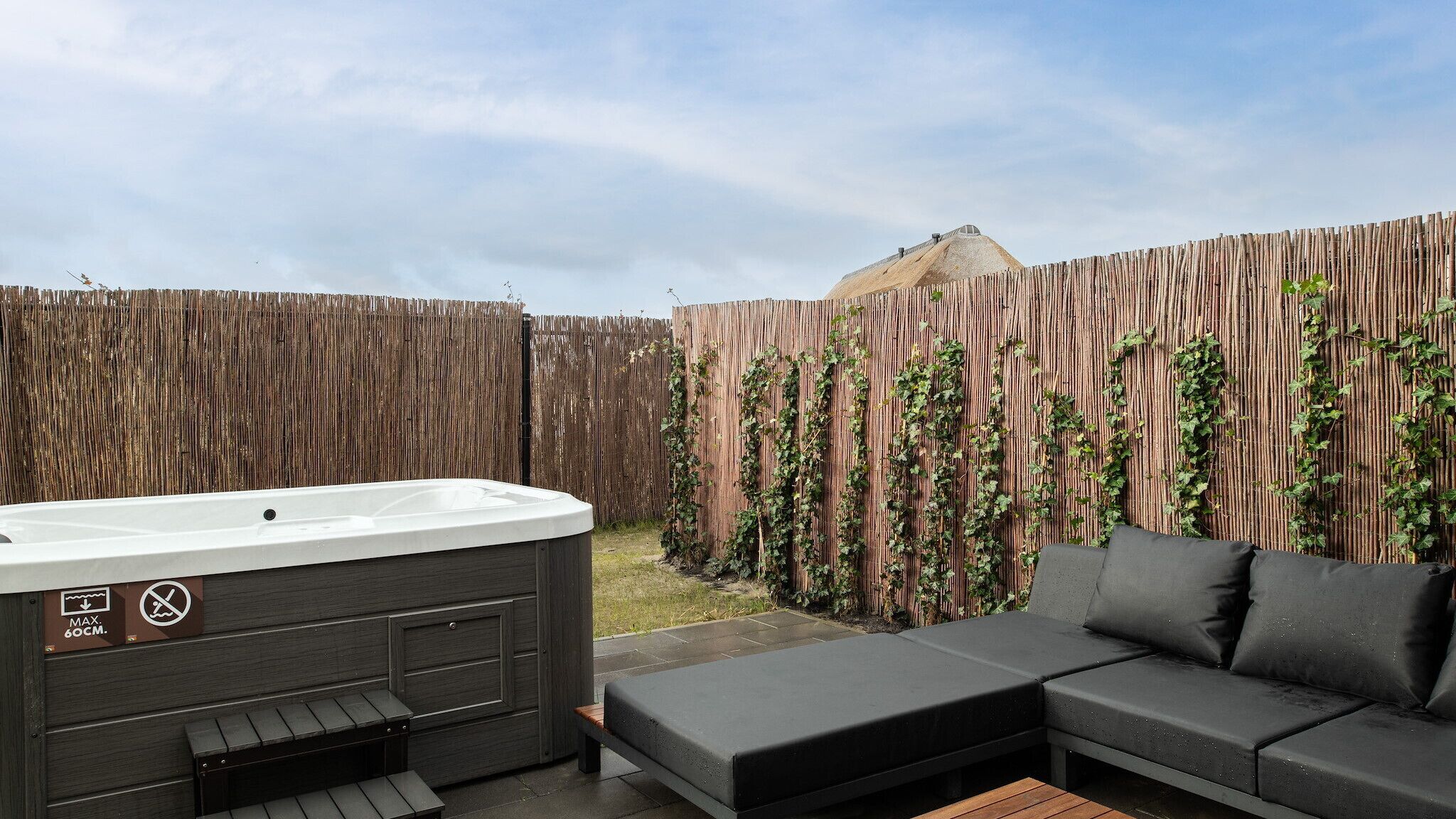 A hot tub, a wooden fence, and a black sofa in a backyard.
